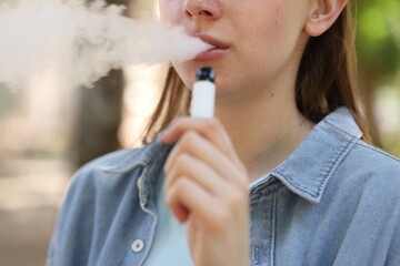 Young woman using electronic smoking device outdoors, closeup