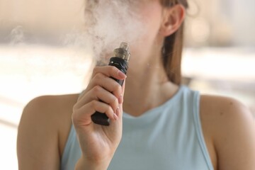 Young woman using electronic smoking device outdoors, closeup
