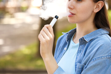 Young woman using electronic smoking device outdoors, closeup