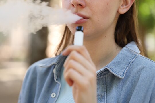 Young woman using electronic smoking device outdoors, closeup - Powered by Adobe