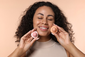 Smiling woman with containers of lip balm on beige background