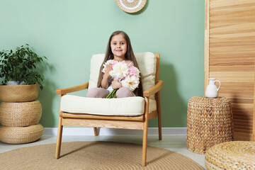 Cute little girl with bouquet of beautiful peonies in armchair near green wall indoors