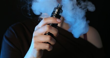 Woman using electronic smoking device in neon lights on black background, closeup