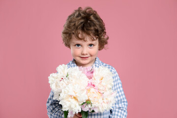 Cute little boy with bouquet of beautiful peonies on pink background