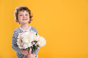 Cute little boy with bouquet of beautiful peonies on yellow background. Space for text