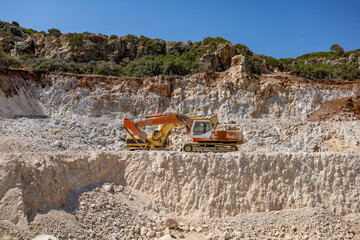 Wide view of two old excavators in a limestone quarry, surrounded by layered rock formations,...