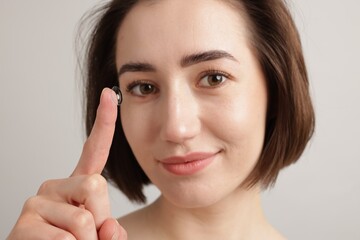 Woman with contact lens on light background, closeup