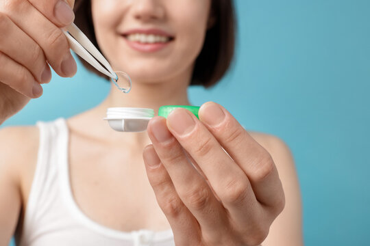 Woman taking contact lens out of case on light blue background, closeup