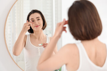 Woman putting in contact lens near mirror indoors