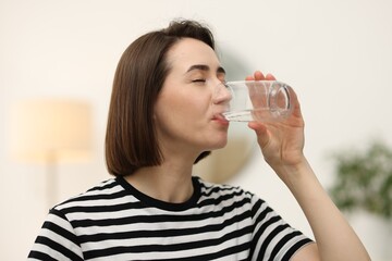 Young woman drinking water from glass at home
