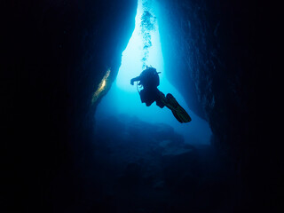diver with flashlight diving between the rocks of an underwater cave, concept of scuba diving and...