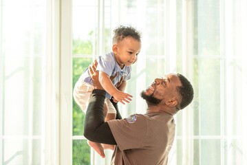 Happy african black parents dad father throw baby son on piggyback and neck riding teasing fun near...