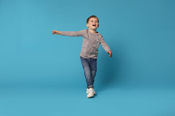 Happy little boy dancing on light blue background