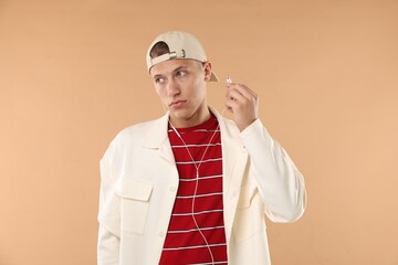 Young man in stylish baseball hat with earphones on beige background