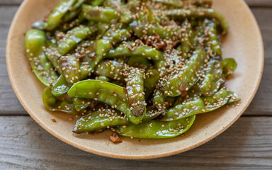 Close up view of Asian Sugar Snap Peas dish. Pea pods stir-fried with garlic, ginger, and soy sauce, and sprinkled with toasted sesame seeds. Rustic wooden table.