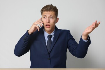Young businessman complaining to someone via phone at wooden table indoors