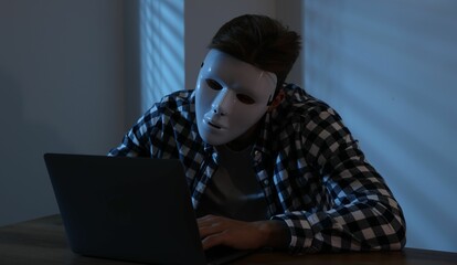 Anonymity. Masked man with laptop at table in dark