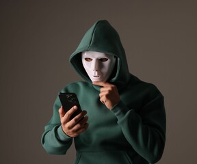 Anonymity. Masked man with smartphone on grey background