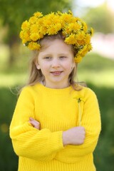 Cute little girl with beautiful flower wearing wreath of dandelions in park