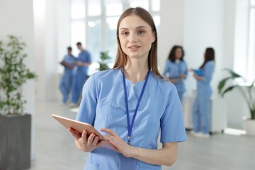 Medical student in uniform with tablet indoors, selective focus