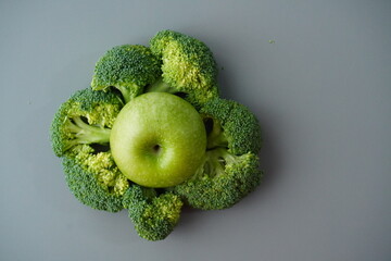 Fresh green apple surrounded by fresh green broccoli on a grey tabletop