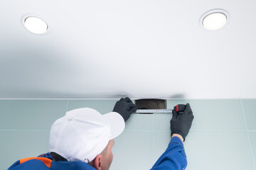 a master in protective uniform and gloves measures the opening of an air duct system, room with a tape measure