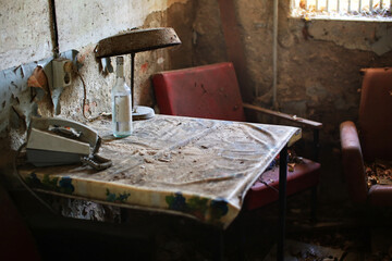 Dusty table with a rotary phone, empty bottle, and rusted lamp in an abandoned interior