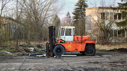Rusty abandoned forklift sitting in an overgrown lot with scattered debris and a decayed building