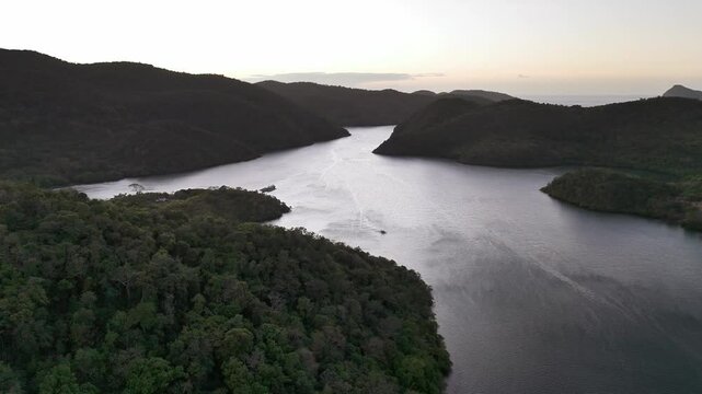 A serene view of Sitio Coring Bay in Western Culion Island, Philippines, surrounded by dense forested hills and calm water, with a boat creating ripples as it moves through the peaceful inlet