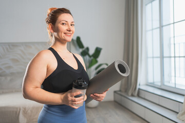 Yoga fitness sport workout training. Woman hold yoga mat bottle water ready for practicing yoga at home. Plus size female doing sports indoor. Girl in sportswear have training workout for weight loss