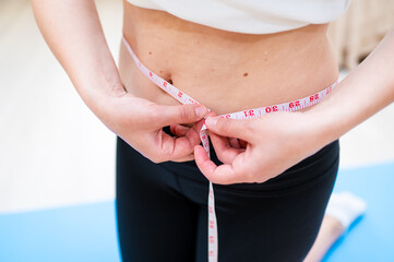 Woman with imperfect waist measuring it with tape while standing on yoga mat, body awareness and...