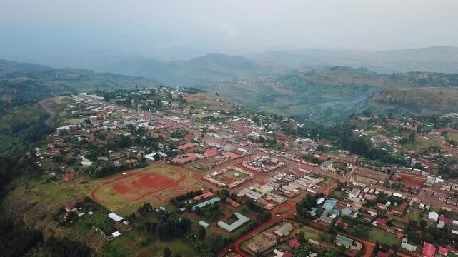Wide drone view of Kapchorwa Town, Eastern Uganda, featuring a prominent red athletics track, surrounding buildings, and lush highland terrain on the slopes of Mount Elgon.