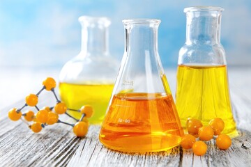 Three glass beakers filled with amber liquid, alongside small, yellow berries and a molecular model, on a light gray wooden surface