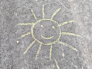 Bright yellow chalk drawing of a cheerful sun with a smiling face on rough asphalt, designed to...