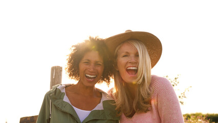 Outdoor Portrait Of Two Mature Female Friends Smiling Into Camera Against Flaring Sun