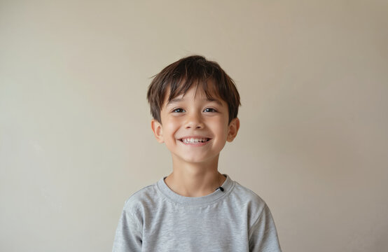 Close-up portrait nine year old boy smiles at camera. Boy with dark hair and brown eyes looks happy. Cute child wears grey t-shirt. Face with kind emotion, perfect smile.