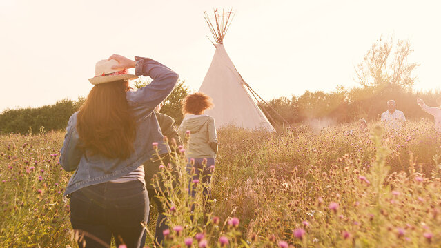 Rear View Of Mature Female Friends Running Through Campsite Field At Sunset