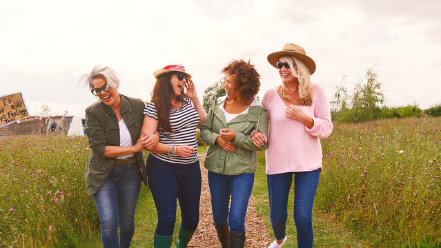 Group Of Smiling Mature Female Friends Walking Arm In Arm Along Path Through Yurt Campsite