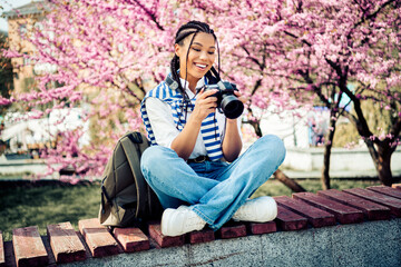 Young woman enjoying leisure time outdoors with a camera during spring afternoon in a blooming park...