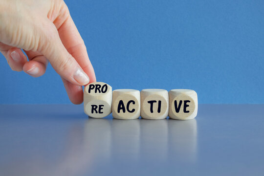 Businessman hand turns cubes and changes the word reactive to proactive. Beautiful blue background, grey table. Business and reactive or proactive concept
