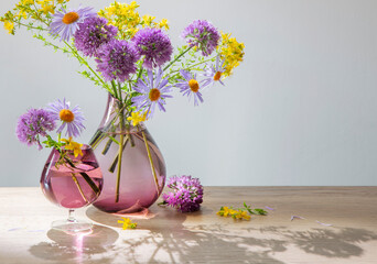 purple and yellow flowers in glass modern vase on wooden table in sunlight
