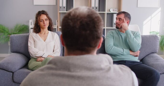 Upset family couple engages in therapy session with psychologist doctor, holding conversation for support and help in a professional setting with focus on consulting and emotional care.