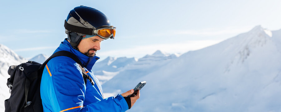 Young adult skier use smartphone make selfie navigate online map app winter alpine skiing resort. Male sporty person with backpack using mobile phone mountain Alps snow slope outdoors cold snowy day - Powered by Adobe