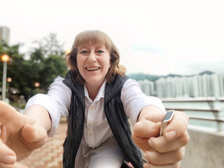 Woman takes a cheerful selfie while exploring Hong Kong's waterfront on a bright day during her...