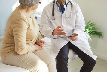 Close-up of male doctor or nurse talking with elderly patient in hospital office, examining and...