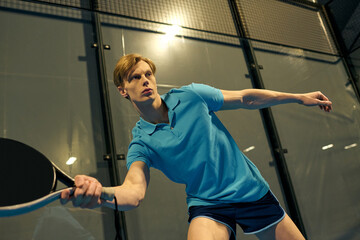 Young sportsman showing skill and focus while playing padel on an indoor court