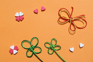 クローバーとハートと蝶の飾りを使った素材　背景オレンジ色　余白あり
