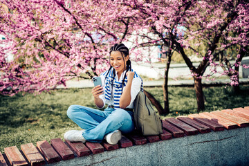 Cute woman with braided hair enjoying a sunny day in a park surrounded by blooming spring trees and...