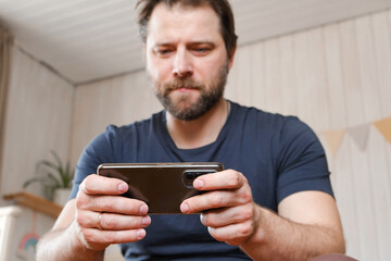 Man using his cellphone. Handsome guy use mobile phone at home. Male browses social networks,...