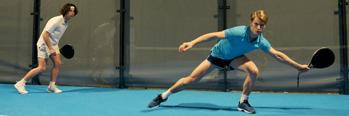 Young sportsmen engage in a thrilling padel match on a vibrant indoor court